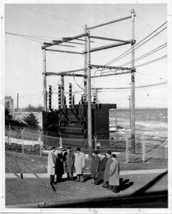 Historical photograph of a group of gentlemen convening beside a newly installed and activated power connector. 