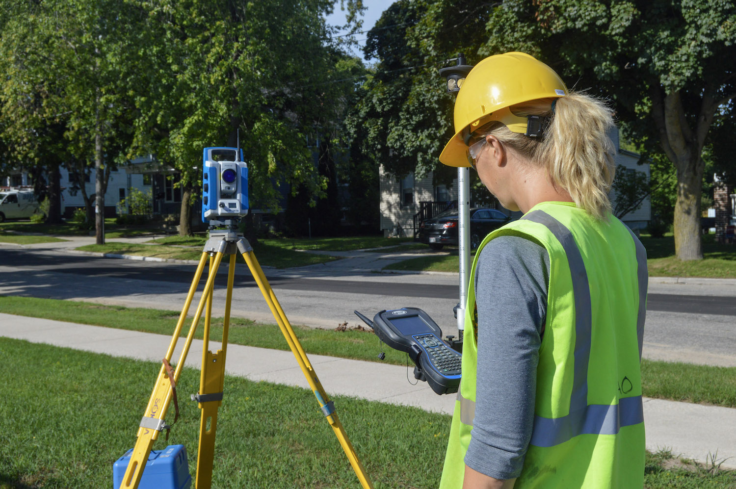 A woman wearing a safety vest and helmet works survey equipment.