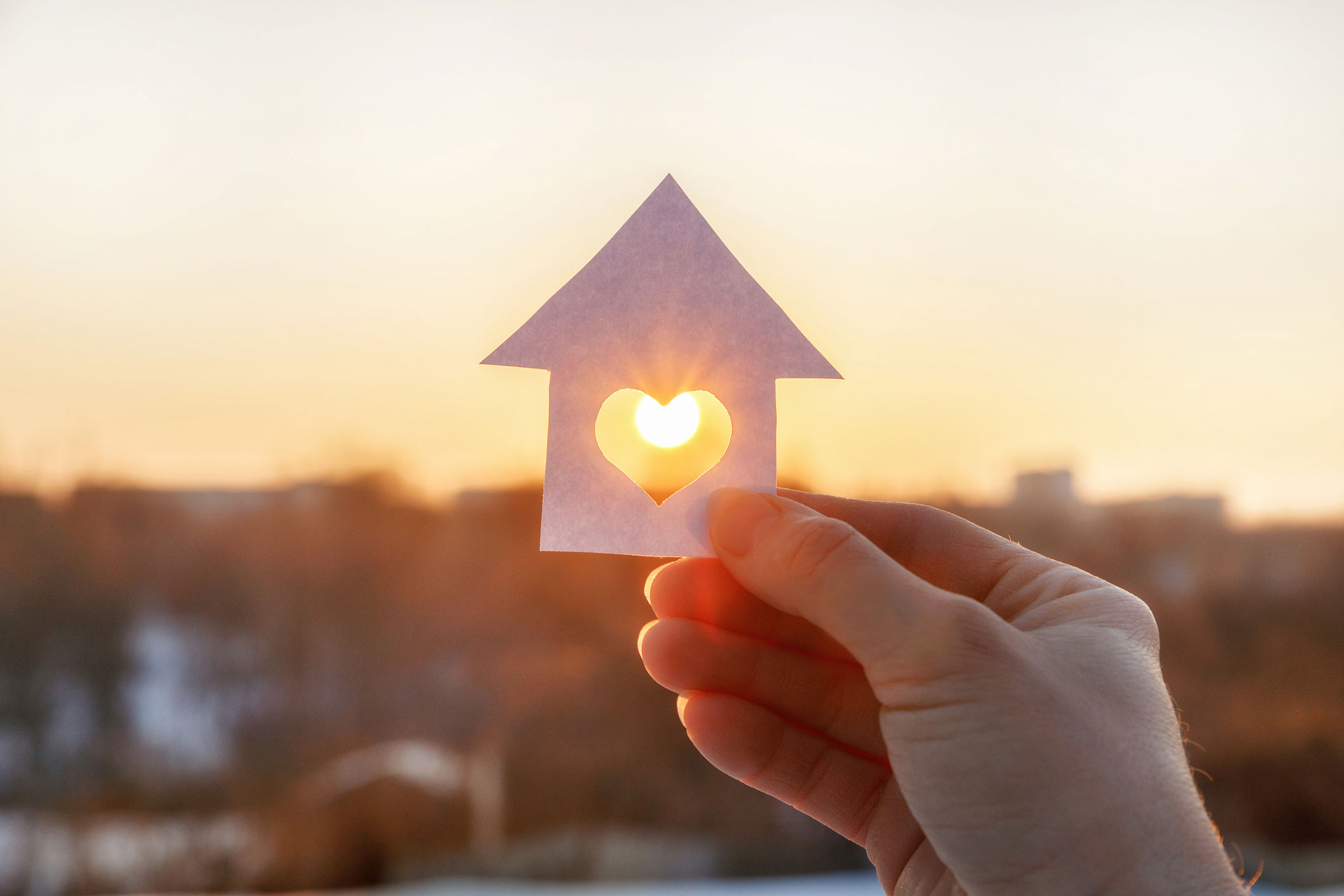 House of paper with a heart in a hand with the rising sun as a background.