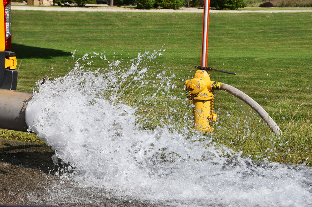 Water flowing from a pipe next to a fire hydrant.