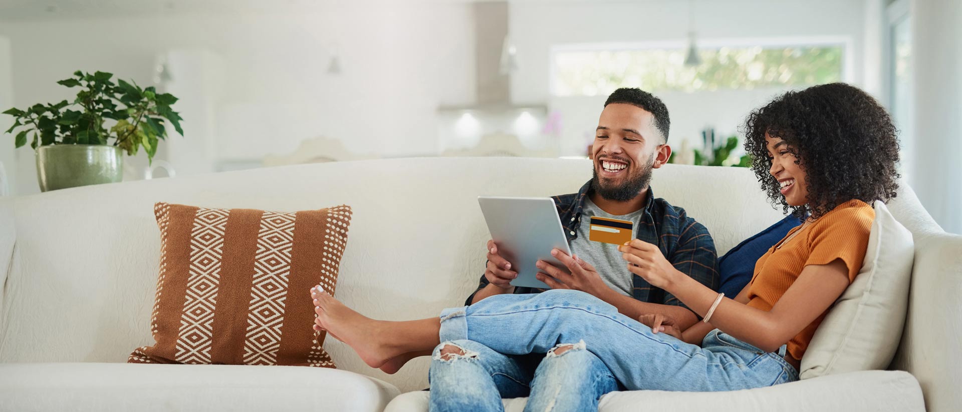 a couple sitting at a couch paying a bill on a tablet