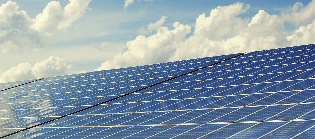 Solar panels in front of a blue sky with fluffy white clouds