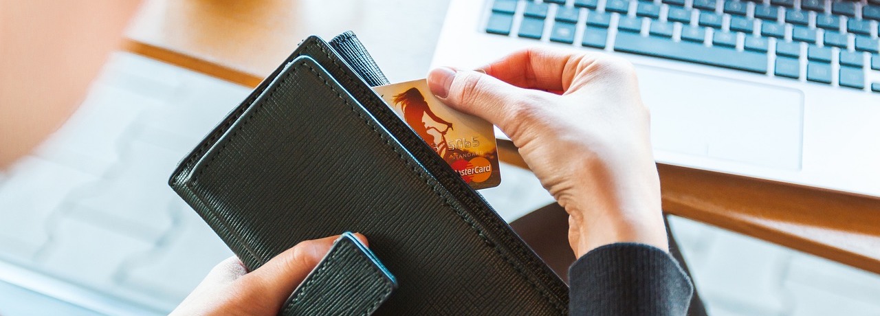 A person removing a credit card from a wallet while sitting at a laptop