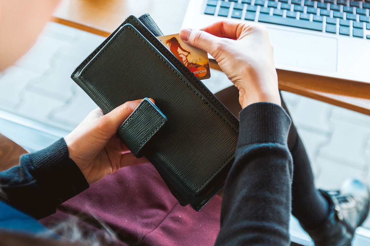 A person removing a credit card from a wallet while sitting at a laptop