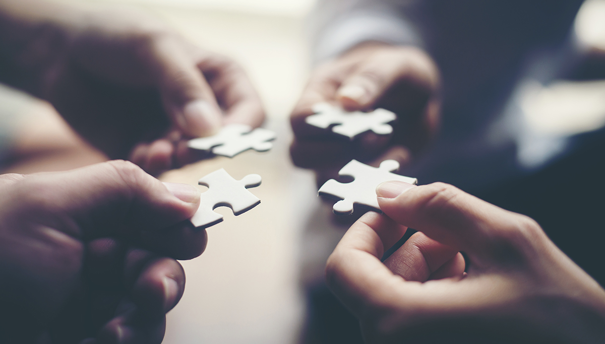 Four hands each holding a piece of a jigsaw puzzle