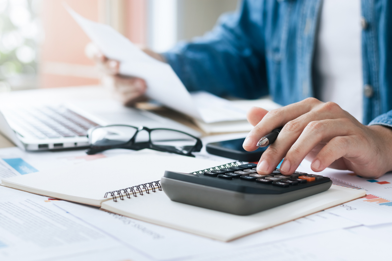 A person sitting at a desk with a calculator and paperwork in front of a laptop