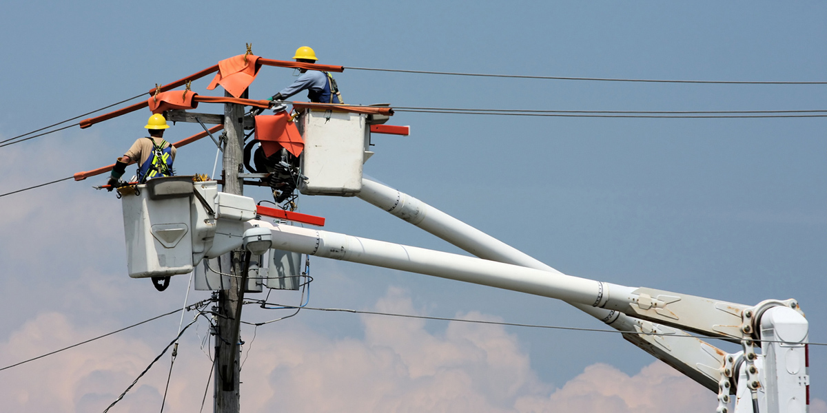 Two workers in a crane repairing a power pole