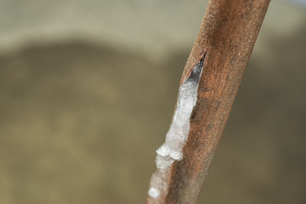 Looking down on a frozen copper water supply line, that has split and leaked water onto the basement floor